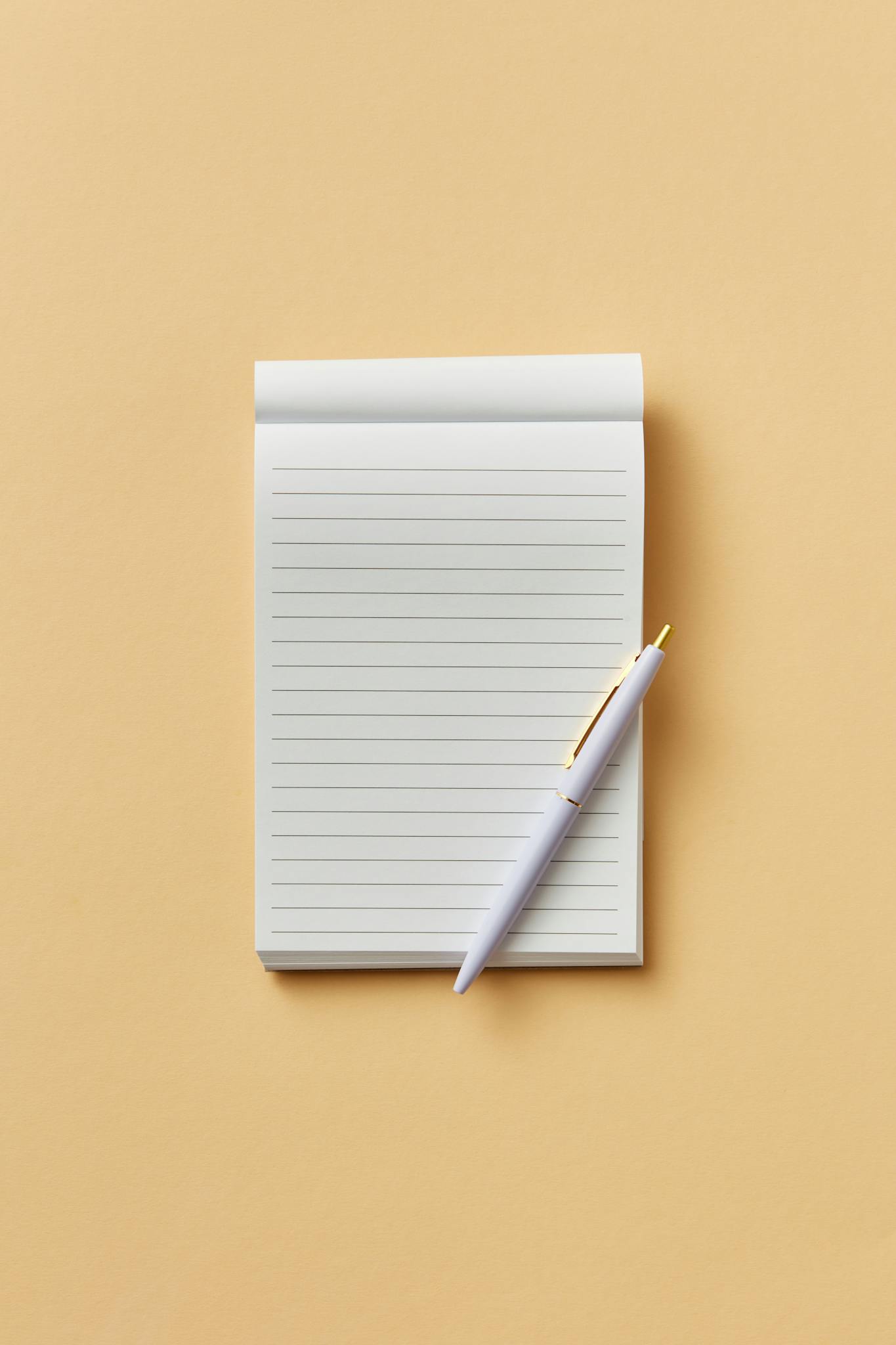 Simple notepad and pen on a beige background, perfect for minimalistic designs and concepts.